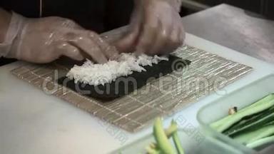 寿司卷的制作和切割过程。 男人用竹垫卷起寿司。 准备好的寿司卷